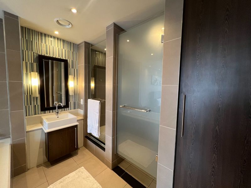 Modern bathroom featuring a vessel sink vanity, walk-in shower with frosted glass door, and contemporary tiled finishes with integrated lighting.