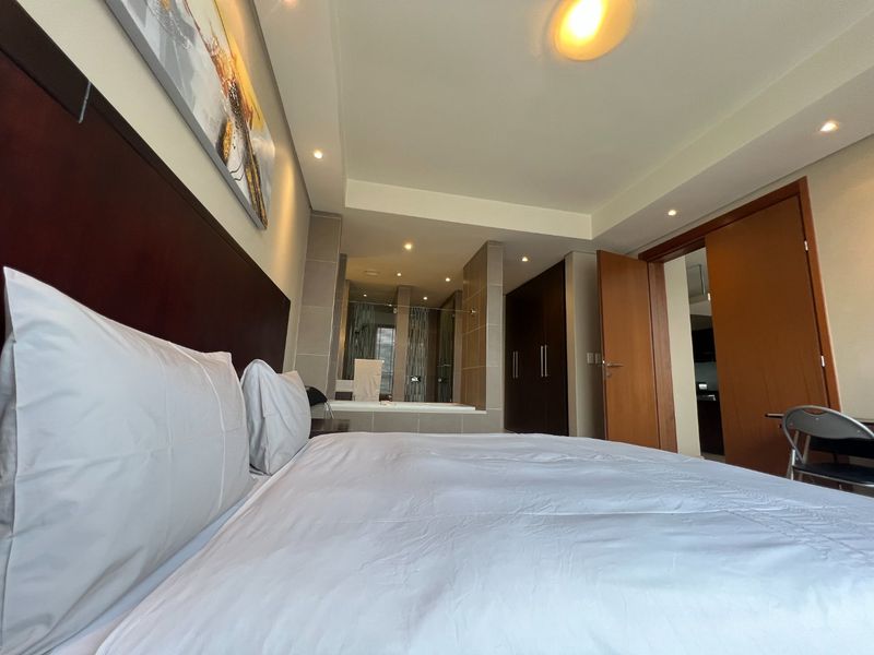 Spacious bedroom featuring built-in cupboards, recessed lighting, and an open-plan en-suite bathroom with a built-in bathtub.
