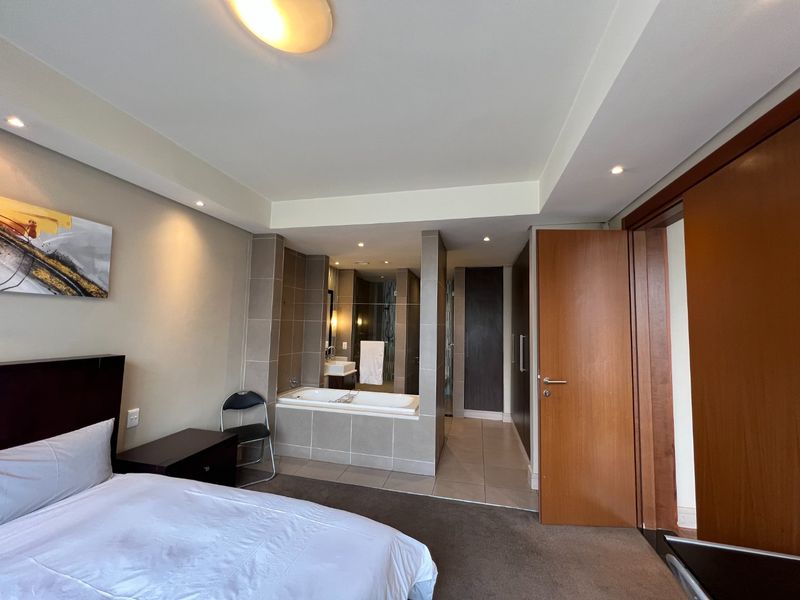 Spacious bedroom featuring an open-plan en-suite bathroom with a built-in bathtub, tiled flooring, and integrated cabinetry.