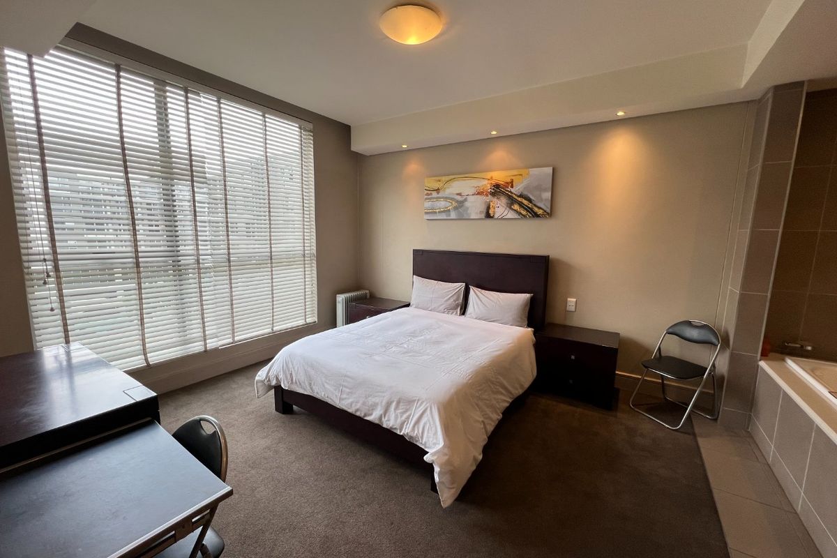 Spacious bedroom featuring carpeted flooring, recessed lighting, large windows with venetian blinds, and an integrated bathtub area.