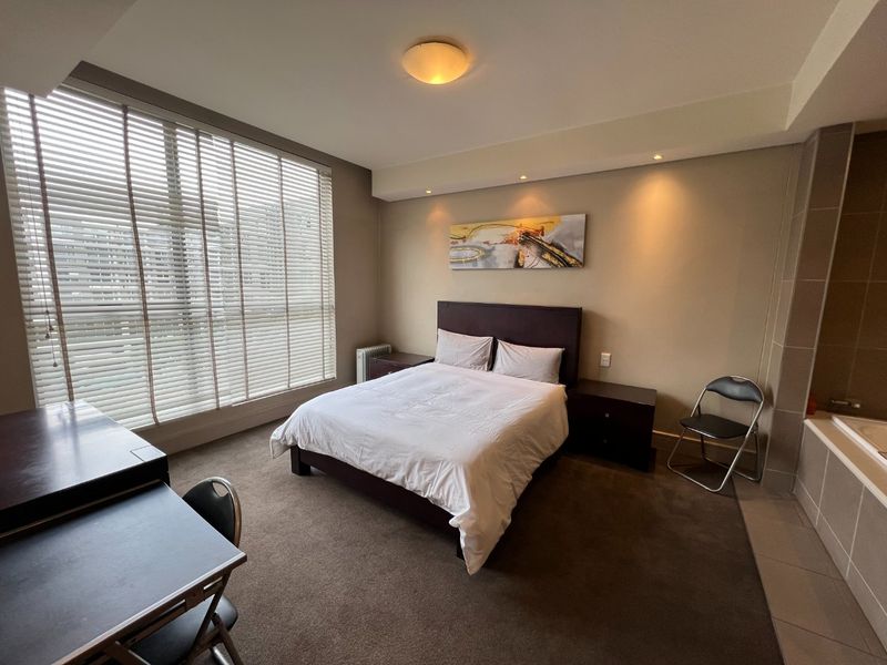 Spacious bedroom featuring carpeted flooring, recessed lighting, large windows with venetian blinds, and an integrated bathtub area.