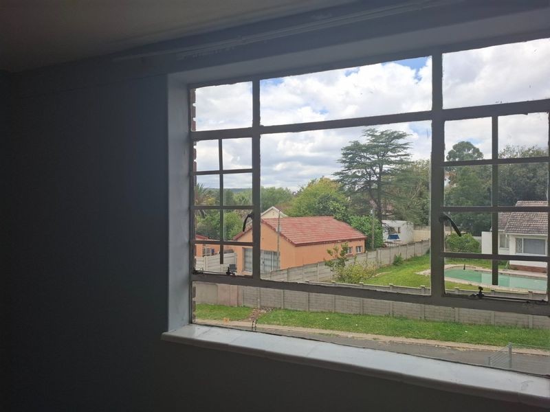An empty bedroom featuring a large steel-framed window with views of the surrounding neighborhood and garden.