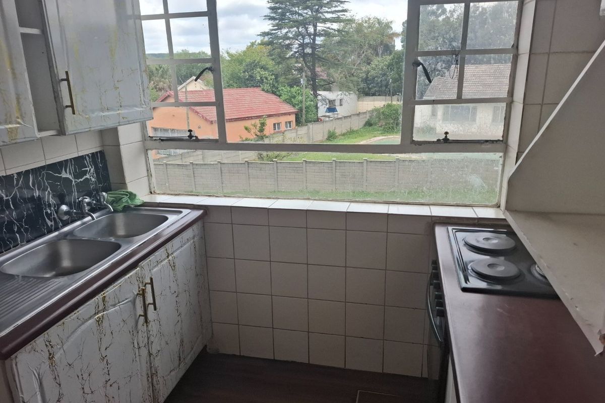 Compact kitchen featuring a double stainless steel sink, built-in cabinetry, and an electric hob, with a large window overlooking the rear garden area.