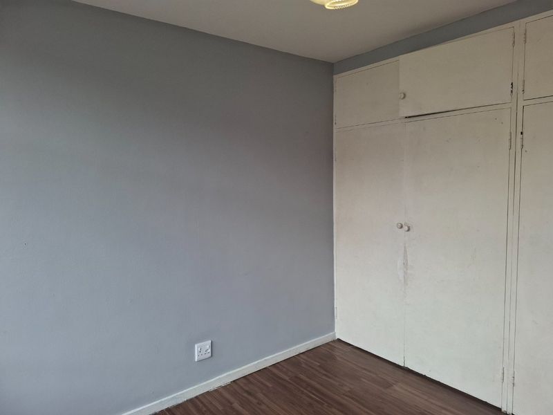 An empty bedroom featuring laminate flooring and built-in cupboards with a neutral grey wall finish.