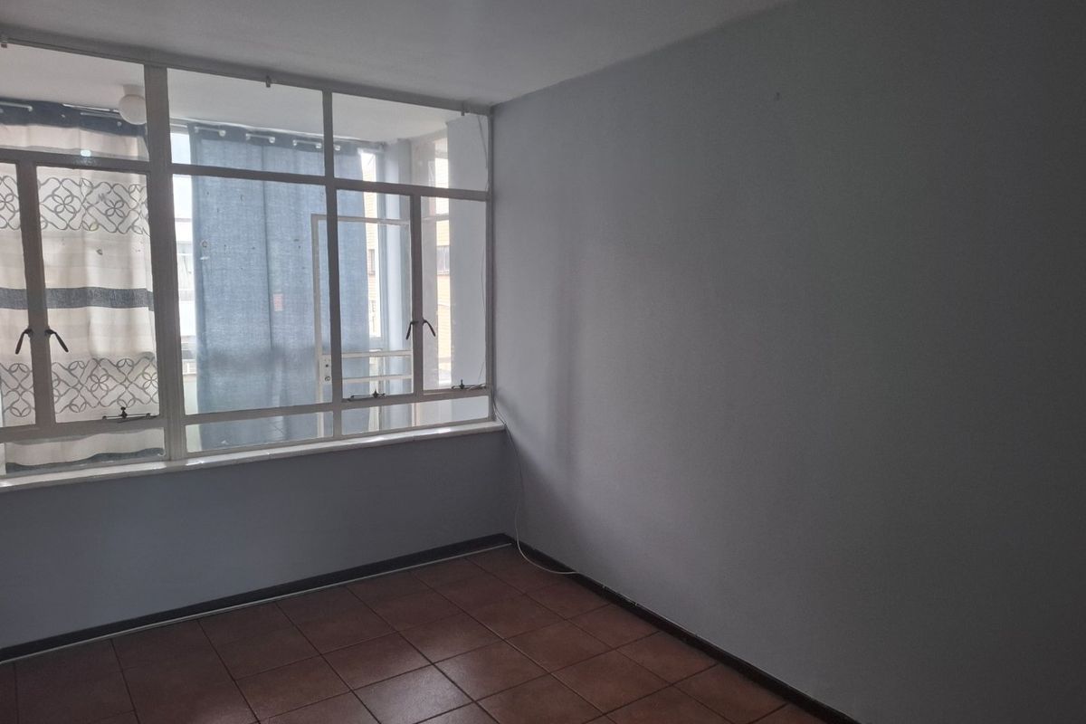 An empty living room featuring large aluminium-framed windows and tiled flooring, offering a blank canvas for interior design.