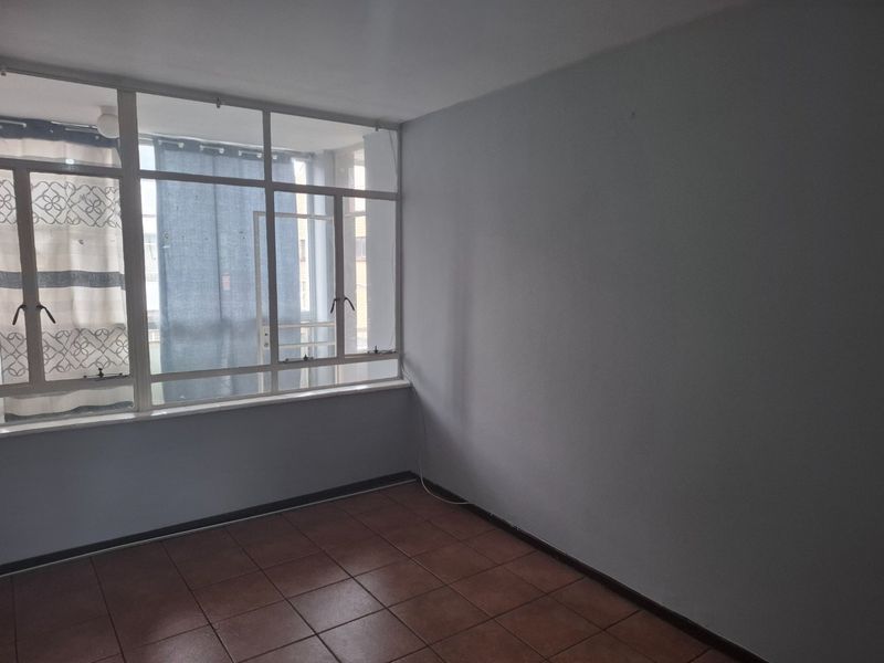 An empty living room featuring large aluminium-framed windows and tiled flooring, offering a blank canvas for interior design.