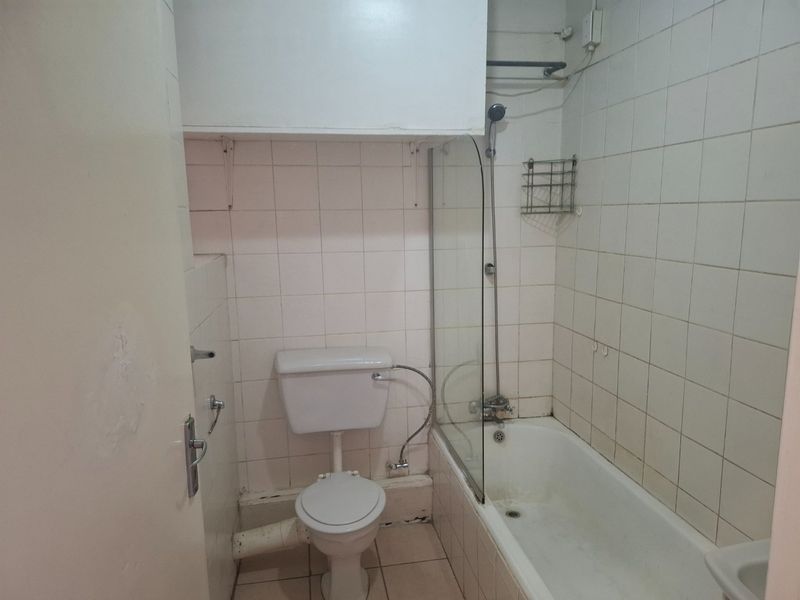 A functional bathroom featuring a bathtub with a glass screen, toilet, and tiled finishes, offering potential for modernization and cosmetic updates.
