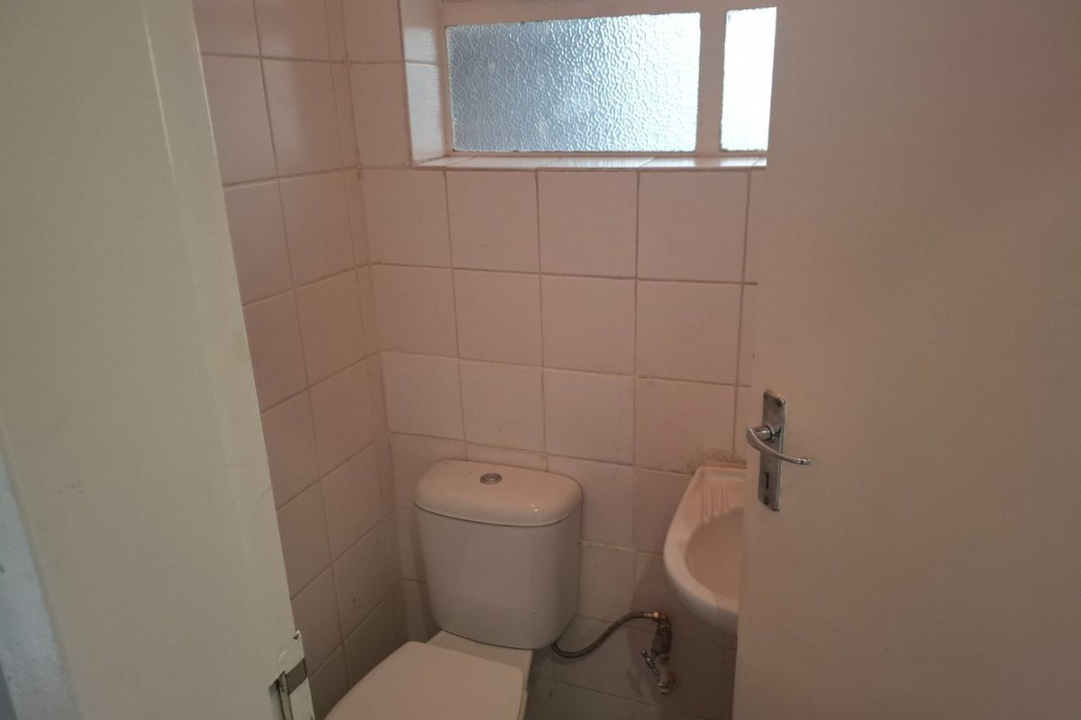 A compact guest bathroom featuring a standard toilet, wall-mounted basin, and tiled walls, requiring cosmetic updates to improve its dated appearance.