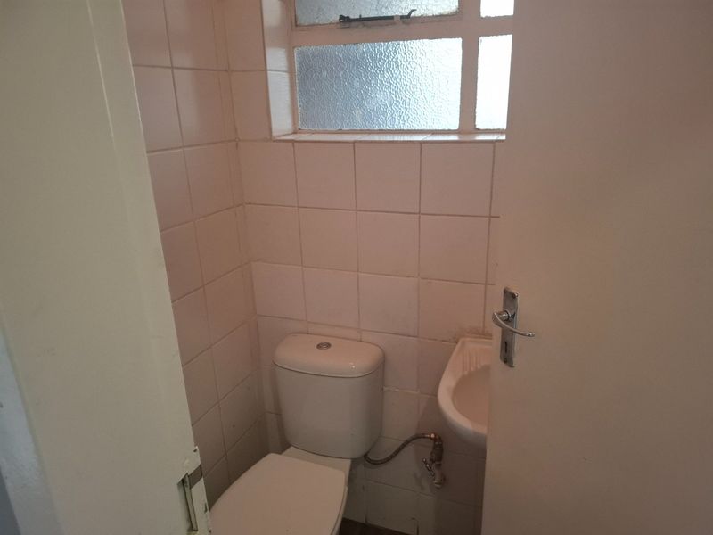A compact guest bathroom featuring a standard toilet, wall-mounted basin, and tiled walls, requiring cosmetic updates to improve its dated appearance.