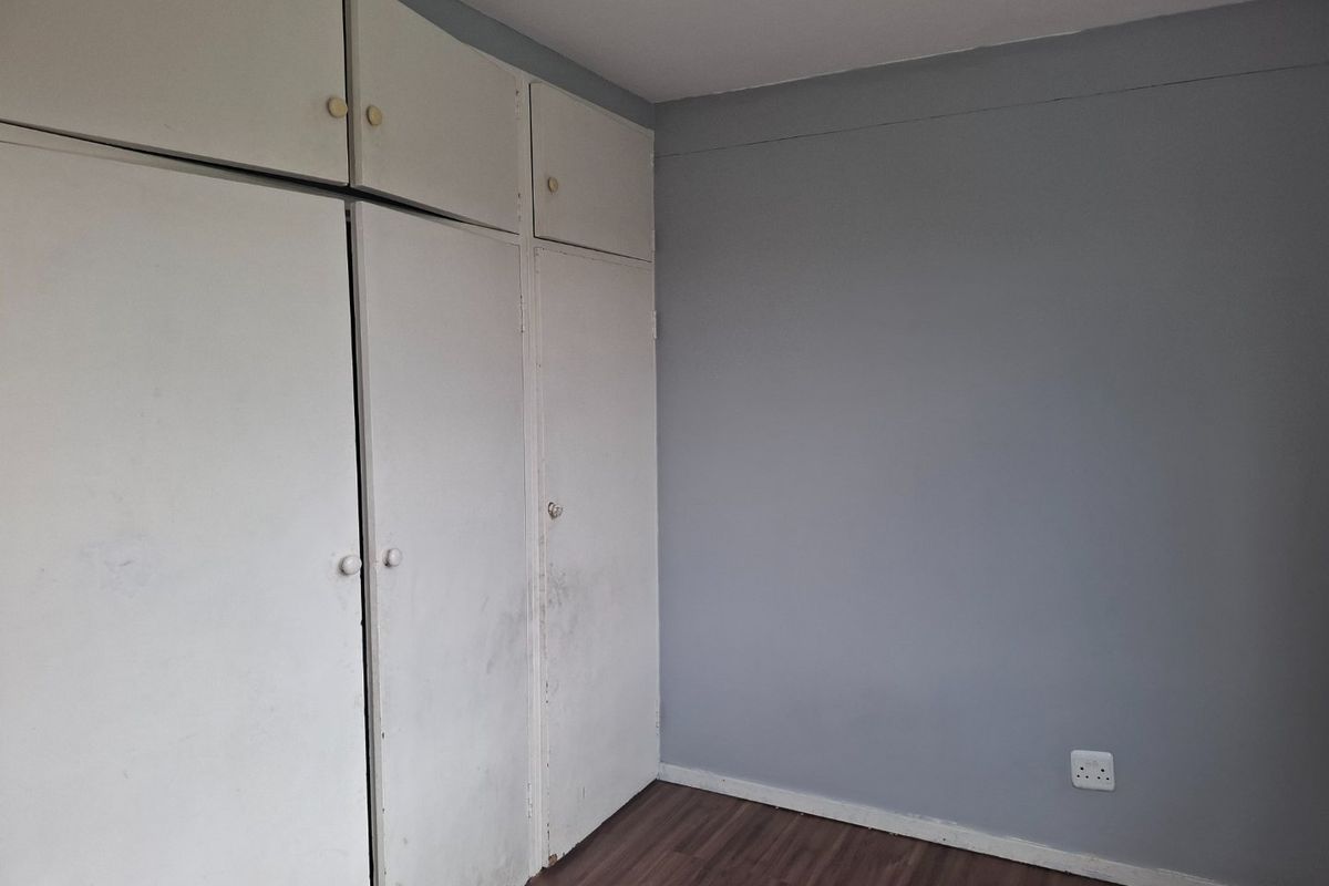 A vacant bedroom featuring laminate flooring and built-in cupboards with a neutral grey wall finish.