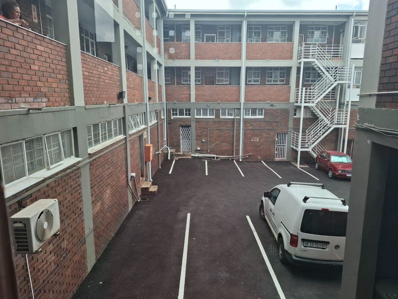 View of the apartment complex rear courtyard featuring exposed brick architecture, an external staircase, and designated asphalt parking bays.