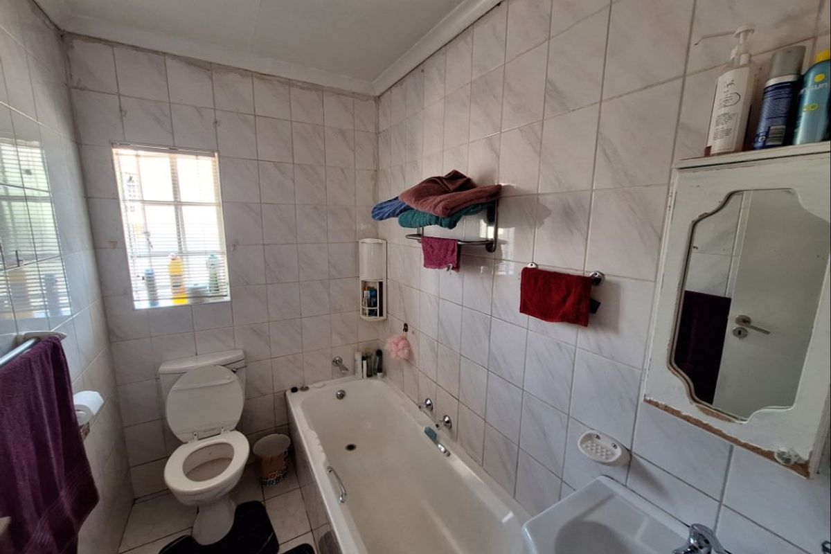 A functional bathroom featuring a bathtub, toilet, and wall-mounted basin with full-height wall tiling and a window for natural light.
