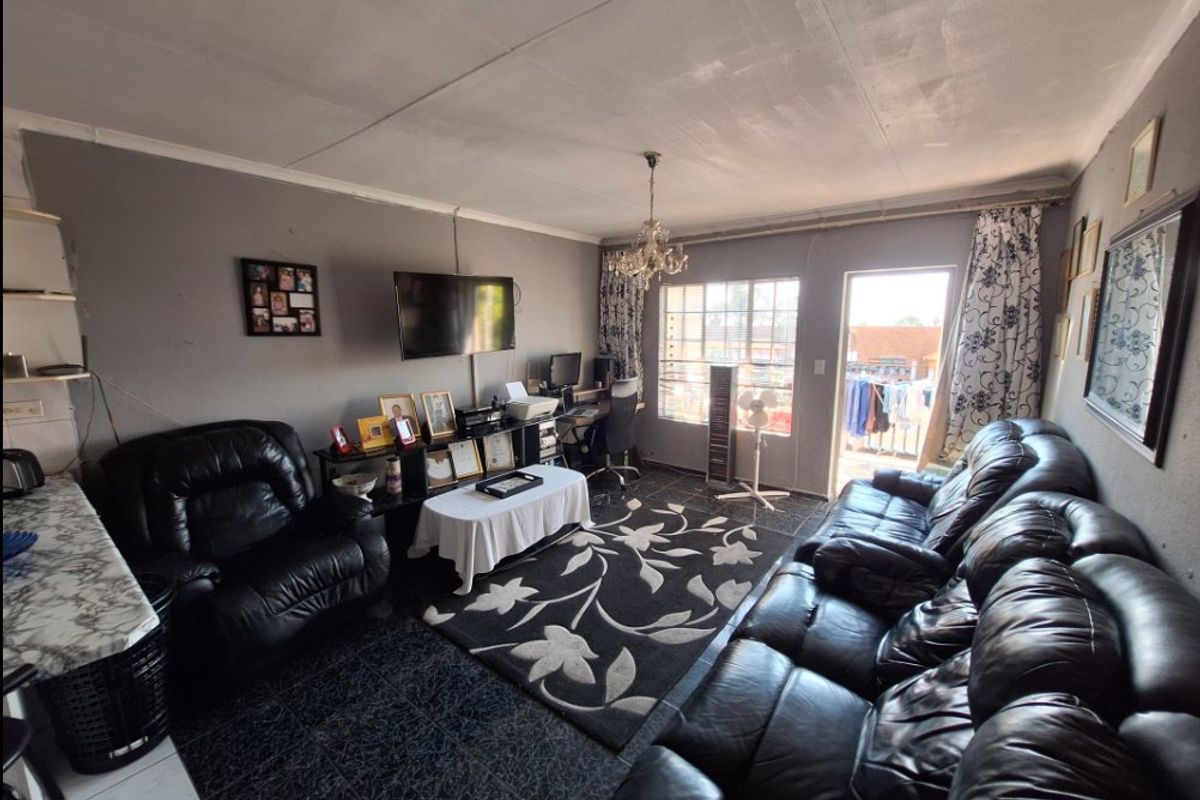 A living room area featuring tiled flooring, a glass door leading to a balcony, and a central ceiling light fixture.
