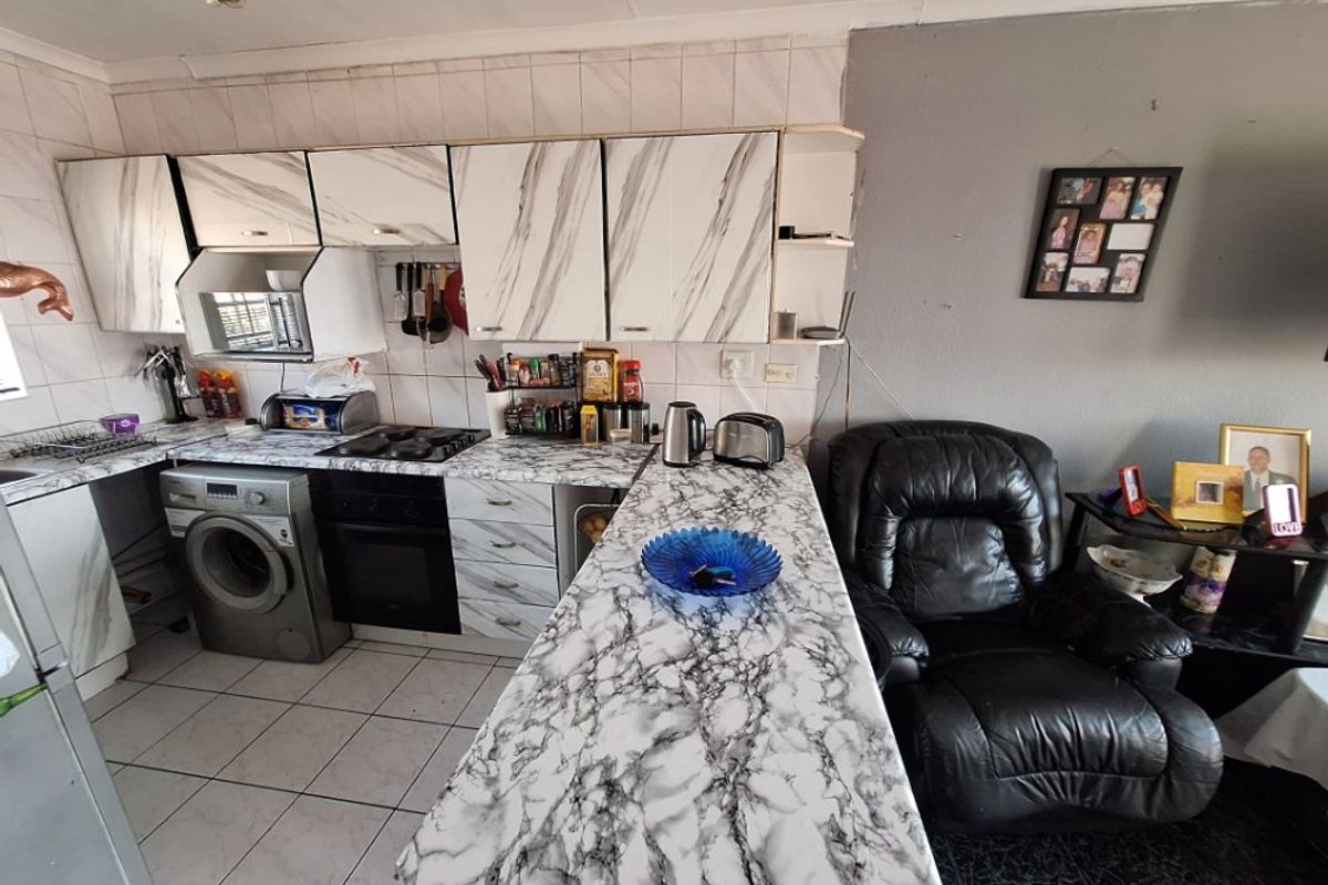 Kitchen featuring marble-effect countertops, built-in oven, hob, extractor fan, and integrated washing machine, with tiled flooring and backsplash.