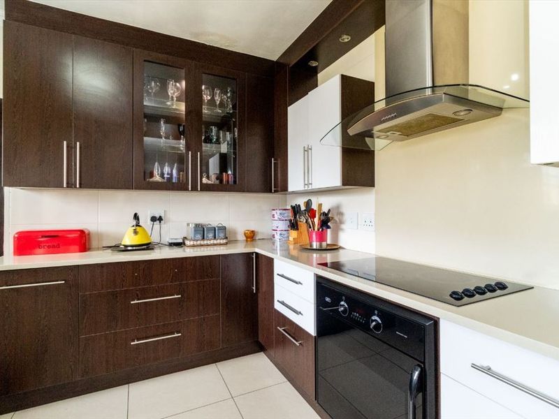 A modern kitchen featuring dark wood and white cabinetry, stone countertops, a built-in oven, glass cooktop, and a stainless steel extractor fan.