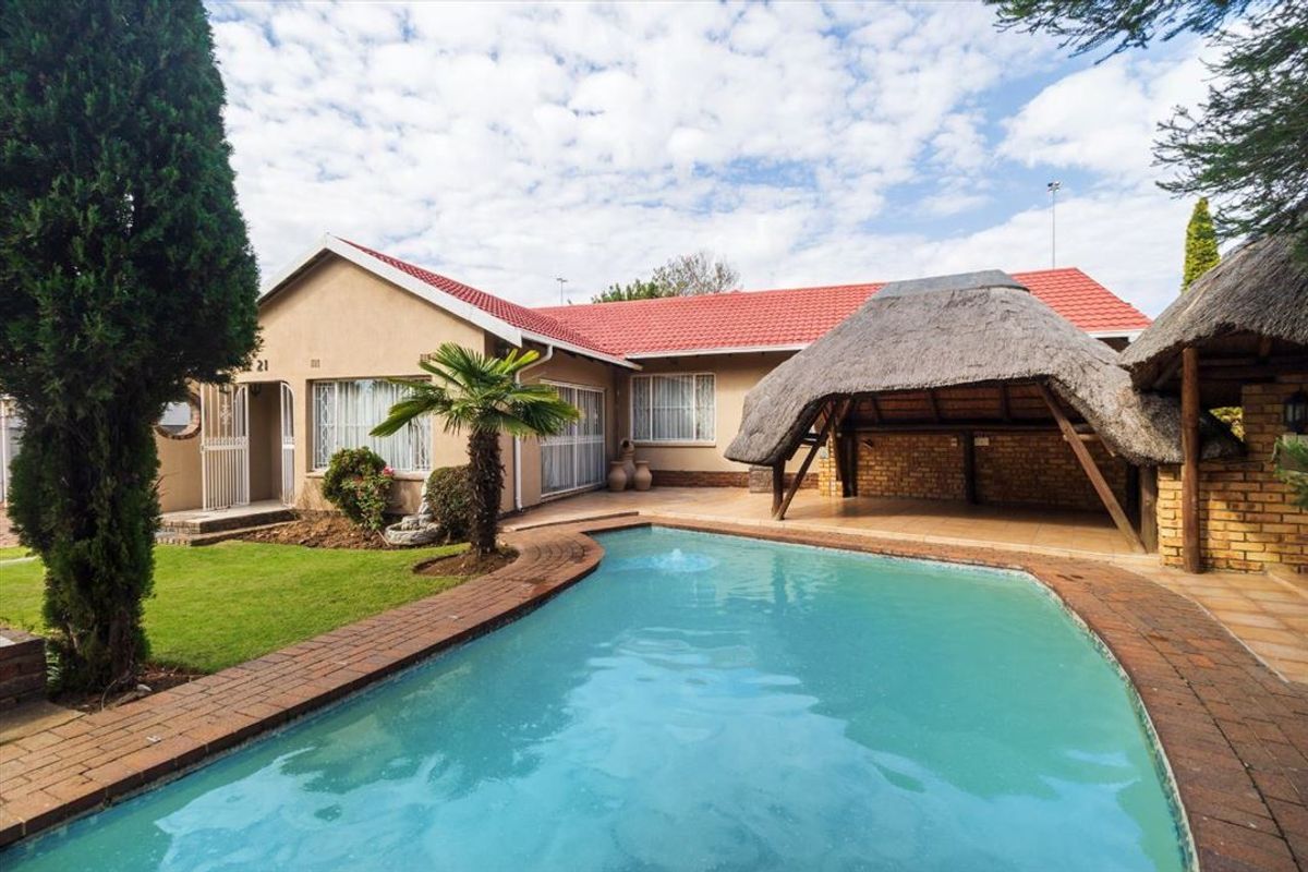 A well-maintained rear exterior view featuring a swimming pool, a thatched lapa entertainment area, and a landscaped garden with a red tiled roof.