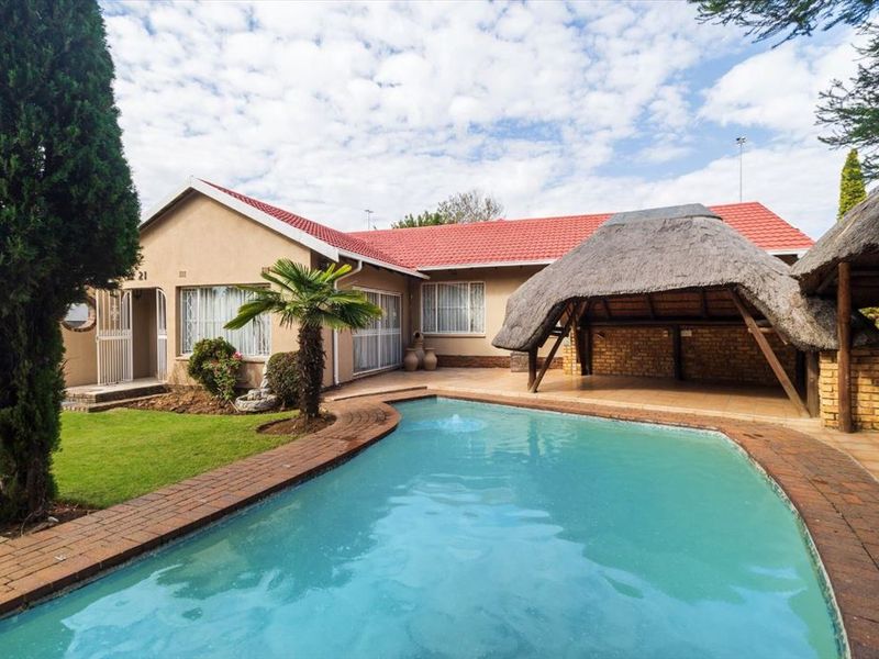 A well-maintained rear exterior view featuring a swimming pool, a thatched lapa entertainment area, and a landscaped garden with a red tiled roof.