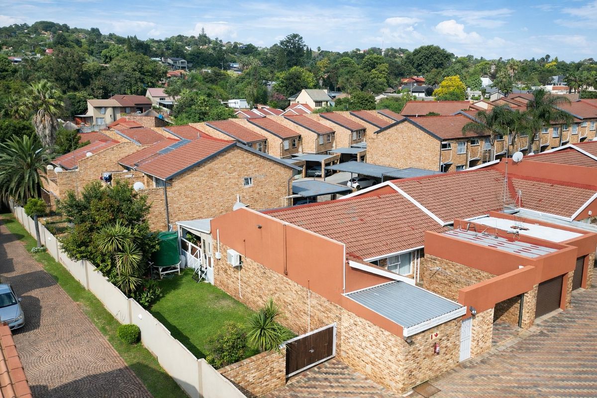 Aerial view of a townhouse complex featuring face-brick exteriors, tiled roofs, paved driveways, and established garden areas.
