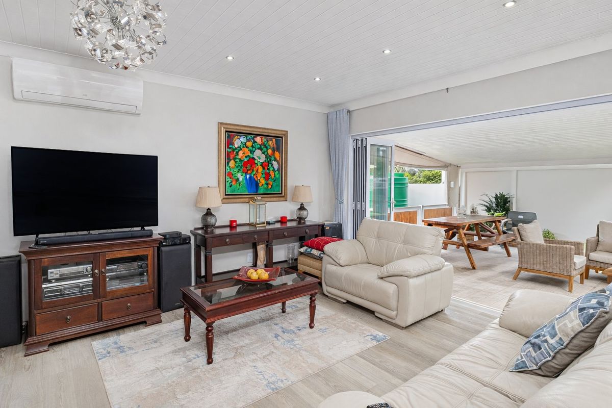 Spacious living room featuring light timber-look flooring, recessed downlighting, and seamless indoor-outdoor flow through bi-fold doors to the covered patio area.
