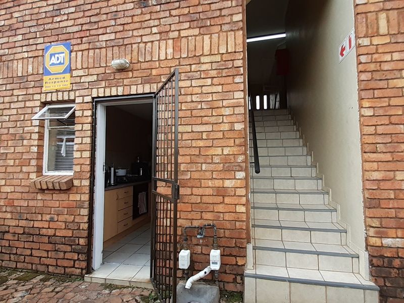 Exterior view of an apartment entrance featuring a face brick facade, security gate, and tiled staircase leading to the upper level.