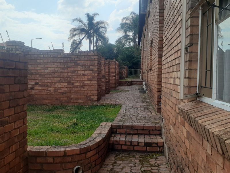 Rear exterior view of the apartment building featuring a brick paved pathway, brick boundary walls, and security features including bars and electric fencing.