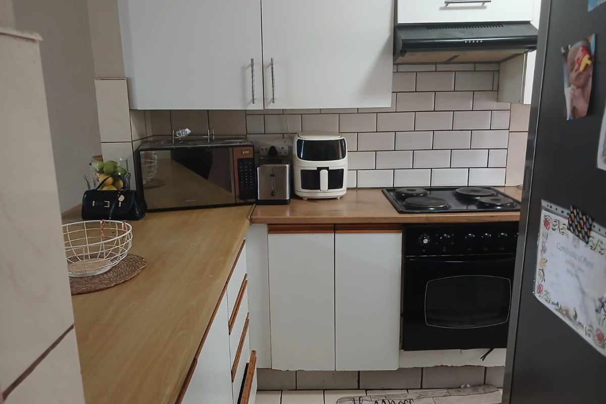 Compact kitchen featuring white cabinetry, wood-look countertops, subway tile backsplash, and a built-in electric oven with hob and extractor fan.