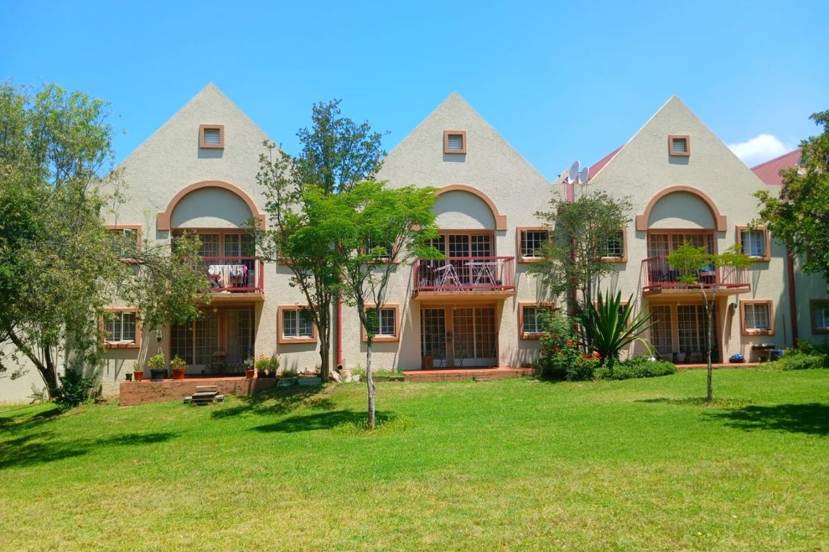 A view of the rear exterior of a multi-unit apartment complex featuring gabled rooflines, private balconies, and a shared garden area.