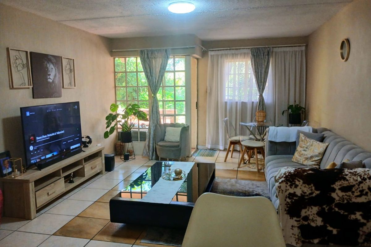 A comfortable living room featuring tiled flooring, large windows providing natural light, and direct access to an outdoor patio area.