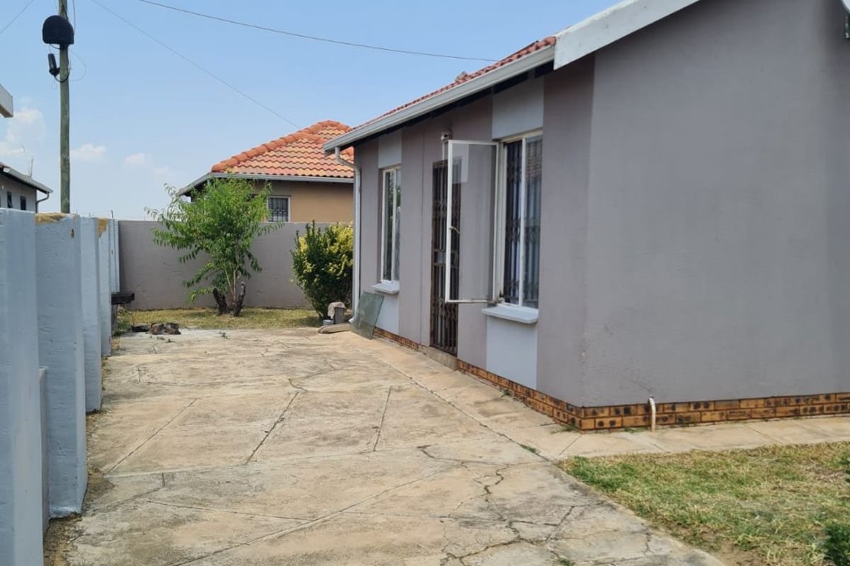 A view of the side exterior of the house featuring a paved walkway, perimeter wall, and established garden area.