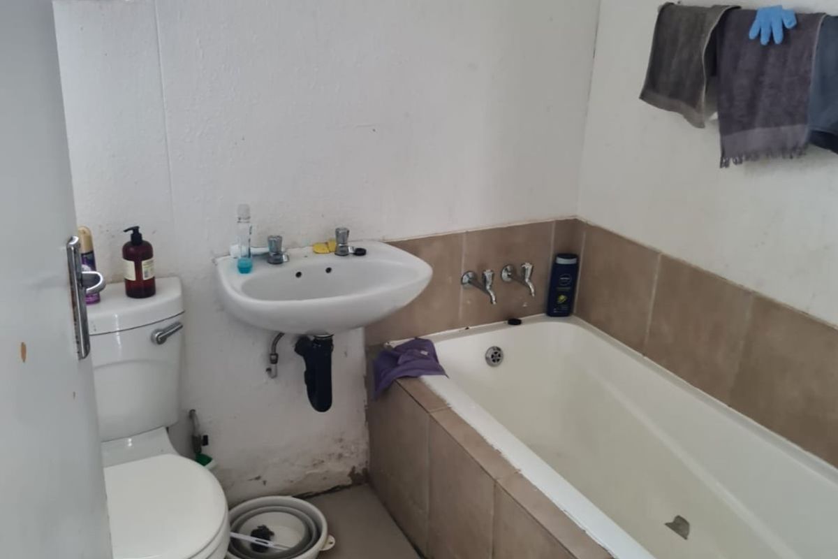 A compact bathroom featuring a standard bathtub with tiled surround, a wall-mounted basin, and a toilet, with a window providing natural light.