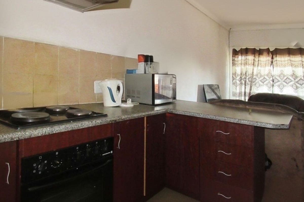 A functional kitchen featuring dark wood cabinetry, laminate countertops, a built-in oven, electric hob, and a tiled splashback.