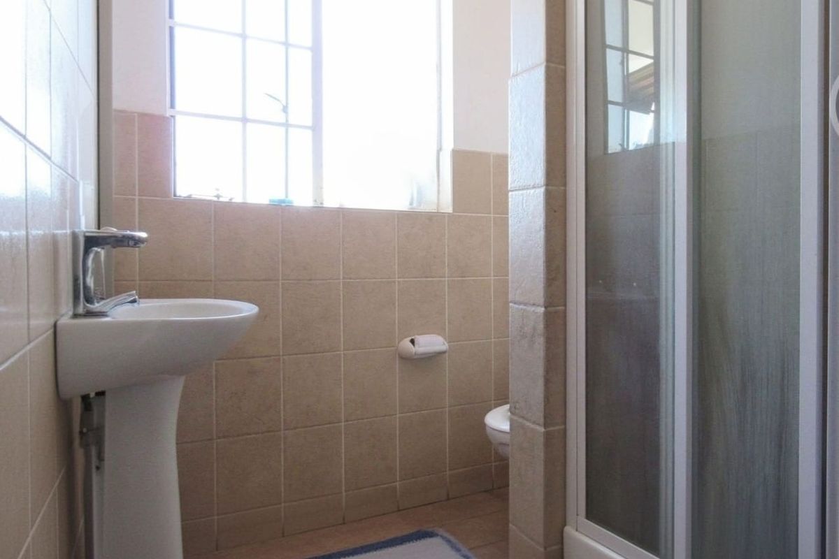 A functional bathroom featuring a pedestal basin, shower enclosure, and neutral ceramic wall tiling.