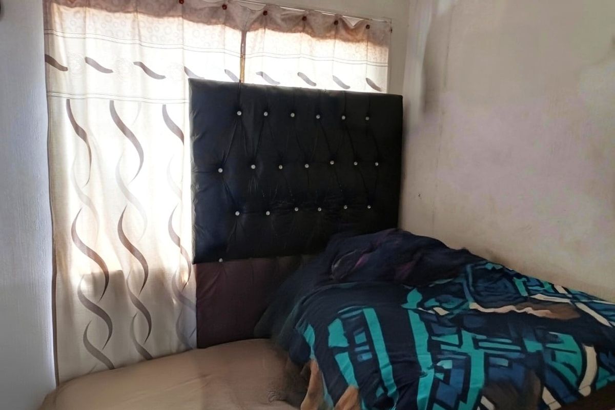 A bedroom interior featuring a window with curtains and visible wall surface wear.