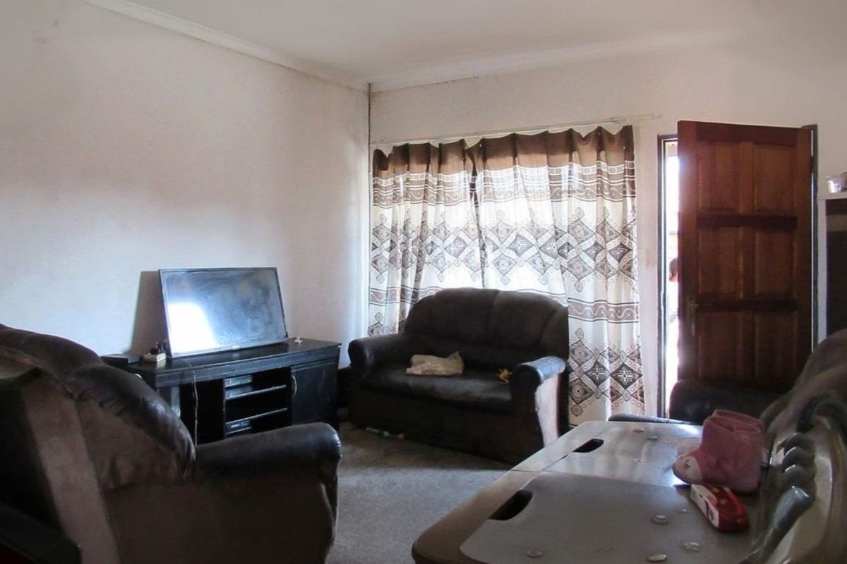 A living room area featuring a timber entrance door and window with curtain rails, requiring cosmetic updates to the wall finishes.