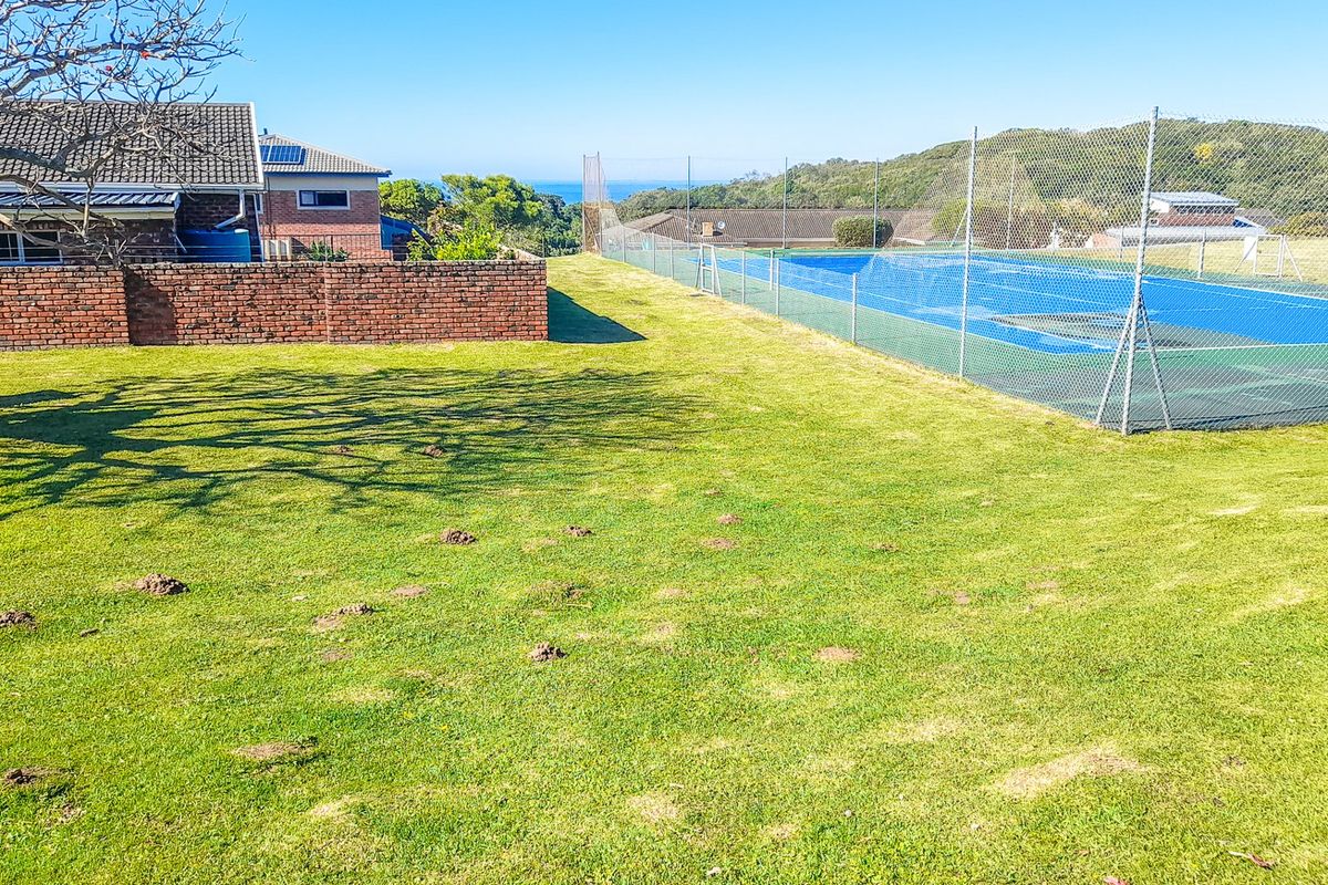 A residential property featuring a private tennis court with chain link fencing, adjacent to a well-maintained lawn and brick boundary wall.