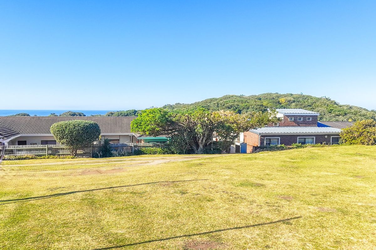 A view of the vacant residential land featuring a grass lawn with surrounding coastal landscape and neighboring properties in the distance.