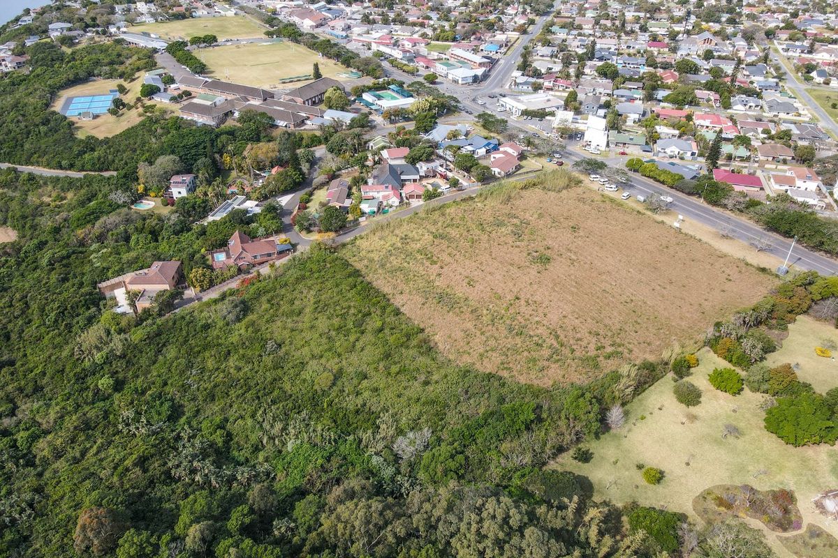 An aerial view of a vacant residential plot situated within an established neighborhood, featuring natural vegetation and proximity to local amenities.