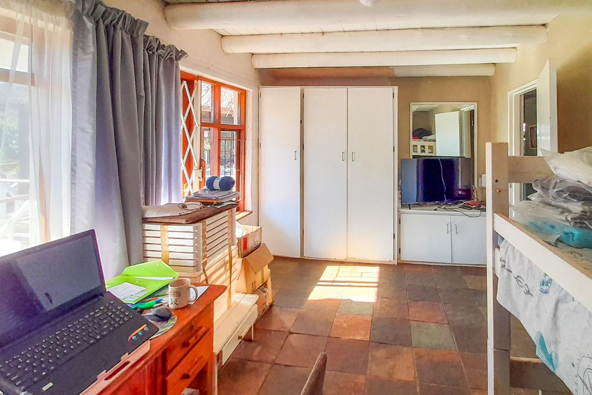 Bedroom featuring exposed timber ceiling beams, tiled flooring, and built-in storage cupboards with natural light from large windows.