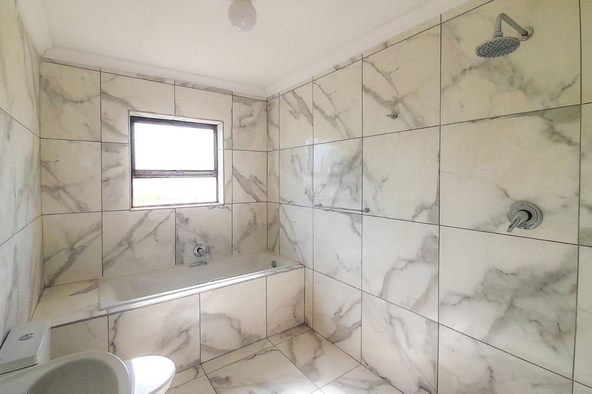 A modern bathroom featuring floor-to-ceiling marble-look tiling, a built-in bathtub, and a separate shower area with contemporary fixtures.