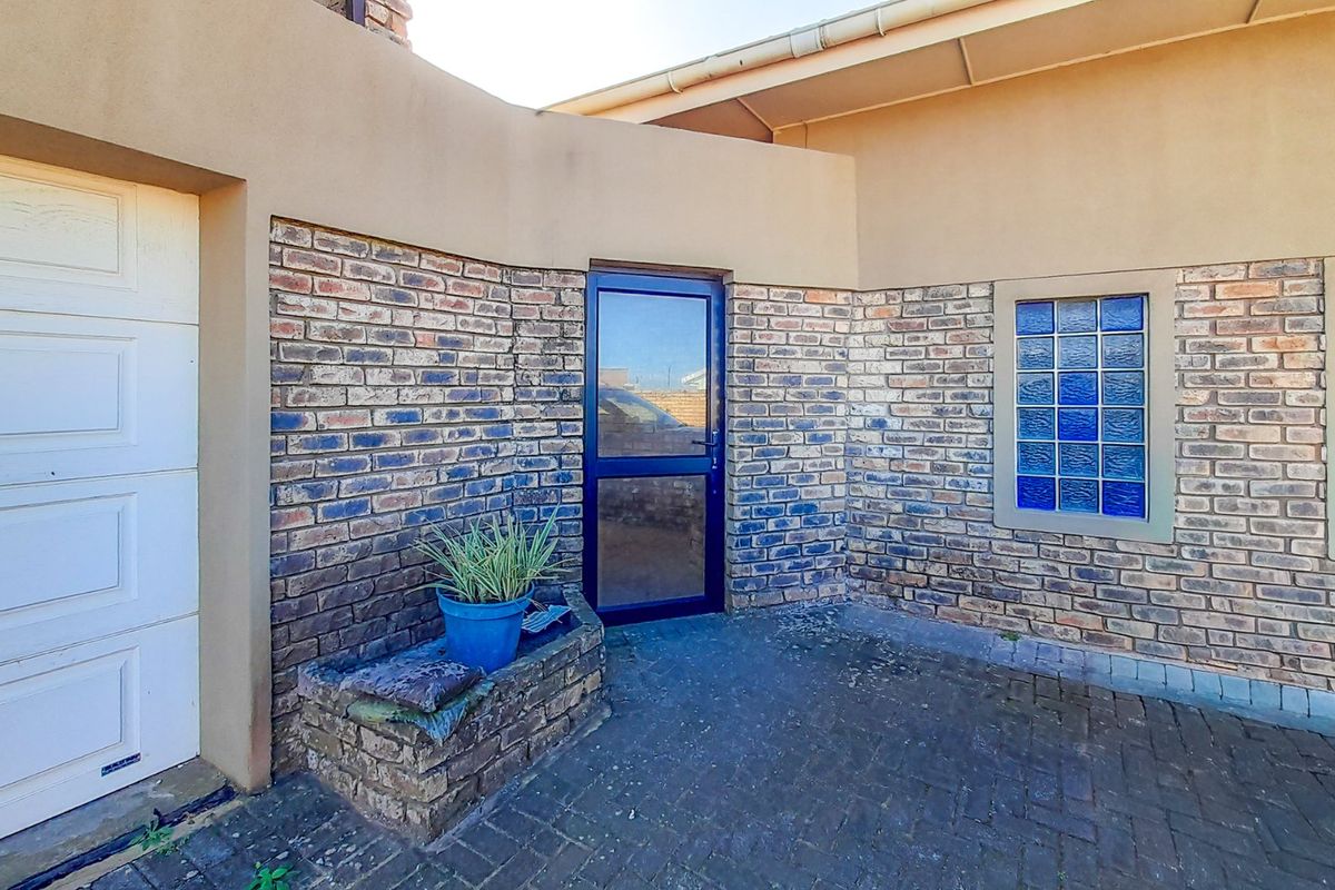 A rear exterior view featuring a paved courtyard area, face brick walls, glass block windows, and access to the garage and main dwelling.