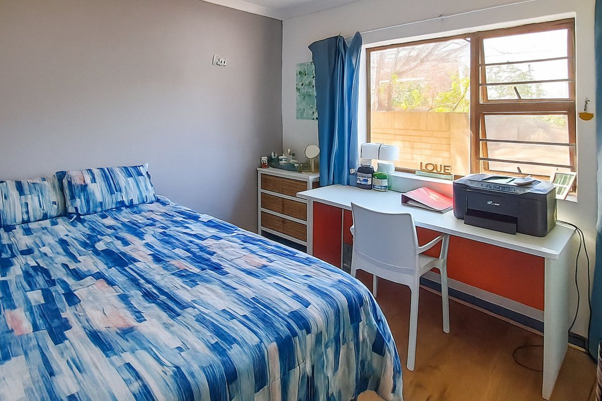 A functional bedroom featuring laminate flooring and a large window with aluminium frames, providing natural light.