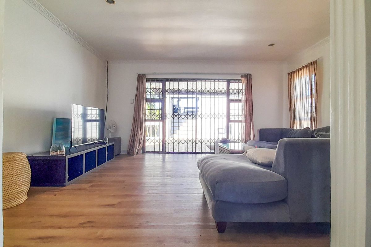 Spacious living room featuring laminate flooring, decorative cornicing, and a large security gate leading to the exterior.