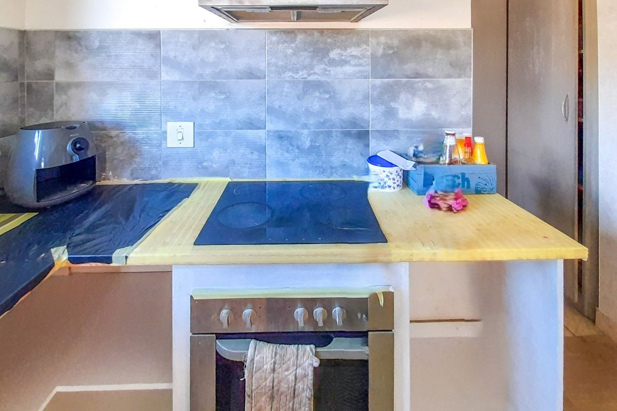 A kitchen area featuring a built-in oven, electric hob, and extractor fan, currently undergoing renovation with unfinished countertops and exposed surfaces.