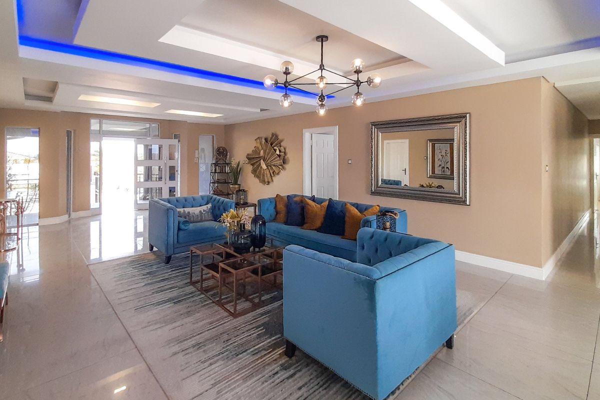 Spacious living room featuring a modern recessed ceiling with integrated LED lighting, a contemporary chandelier, and polished tiled flooring.