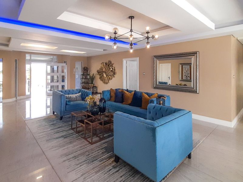 Spacious living room featuring a modern recessed ceiling with integrated LED lighting, a contemporary chandelier, and polished tiled flooring.
