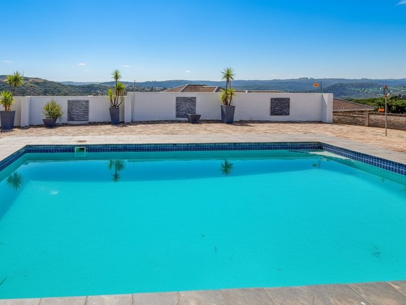 A well-maintained swimming pool area featuring a tiled surround and a boundary wall with decorative stone cladding, offering expansive landscape views.