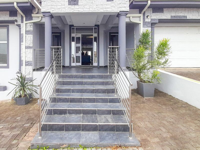 Front entrance of the house featuring a tiled staircase with stainless steel balustrades, stone cladding accents, and a paved driveway leading to the garage.