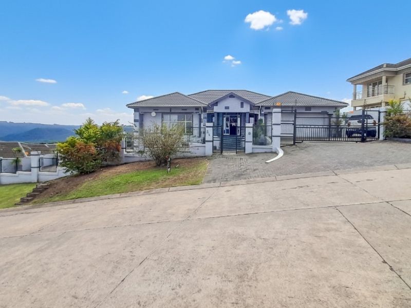 Front elevation of a single-story residential house featuring a paved driveway, secure gated entrance, and tiled roof, situated on a sloped lot.