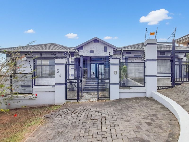 Front elevation of a well-maintained house featuring a paved driveway, secure gated entrance, and electric fencing.