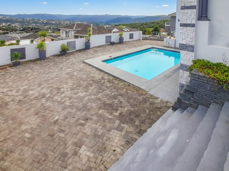 Outdoor pool area featuring a paved patio, stone-clad retaining walls, and concrete stairs, offering expansive elevated views of the surrounding neighborhood.
